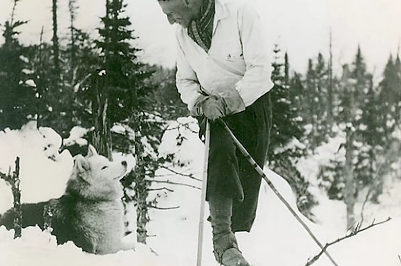 a man looks down at a dog in the snow 