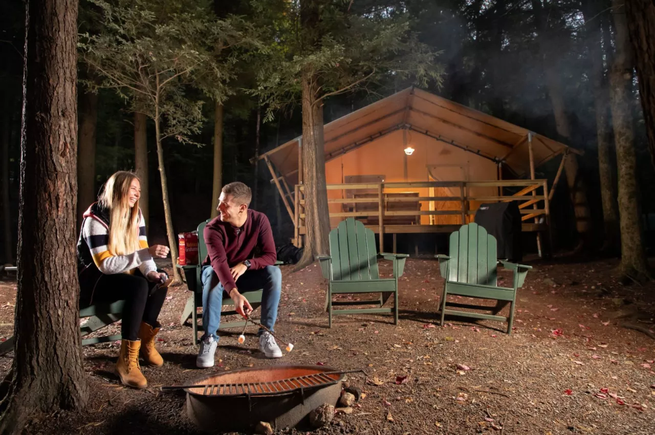A couple sit near a fire outside of a rustic cabin