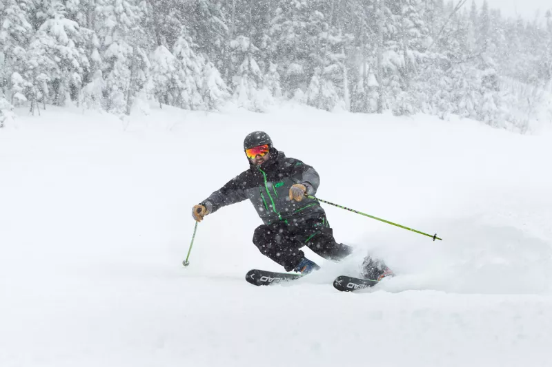A man in a grey snowsuit skis through the falling snow.