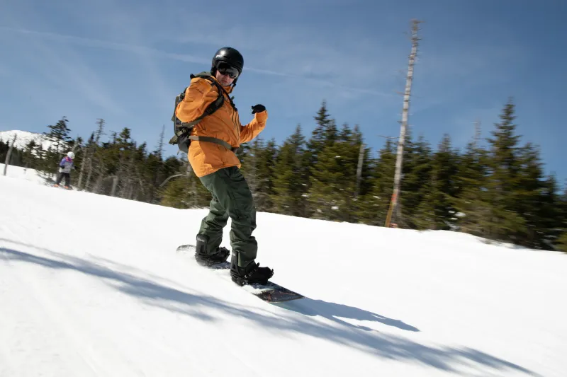 A snowboarder with an orange jacket poses for the camera as they ride down the mountain.