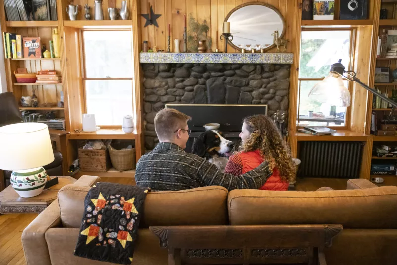 A man and woman sit on the couch facing a fireplace in the living room space at Whiteface Farm