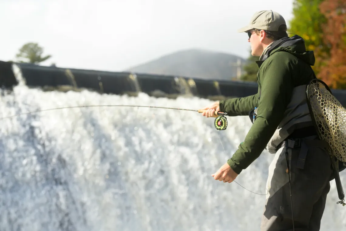 A fisherman casts into the water below a dam
