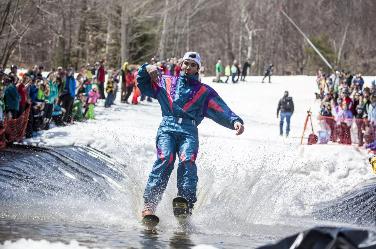 A man skis across a water puddle on the snow in an 80's outfit. 