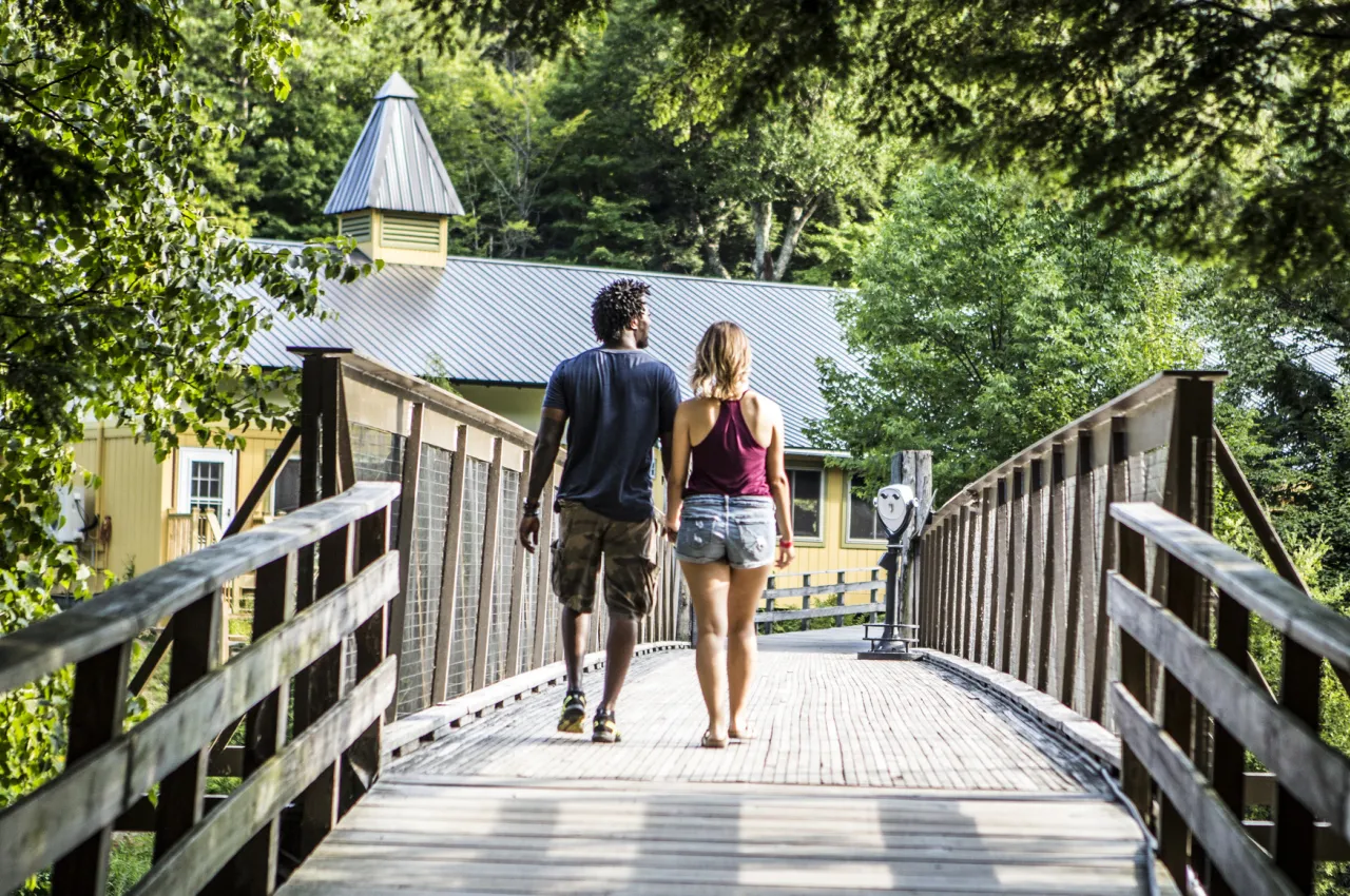 A couple walks across a wooden bridge.