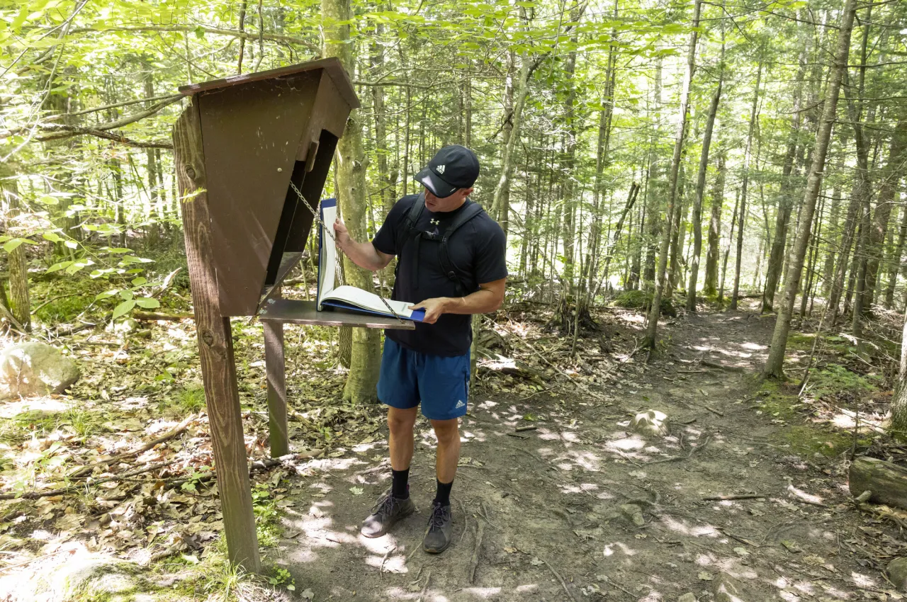 A hiker signs into a trail register