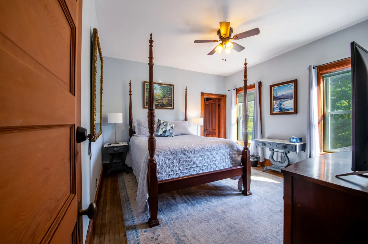 View through a door into a bedroom with four poster bed and lots of nature light through windows