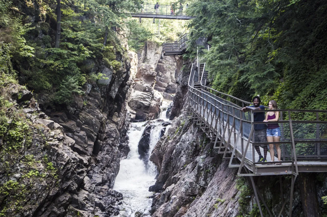Couple stands on elevated boardwalk above waterfall and river