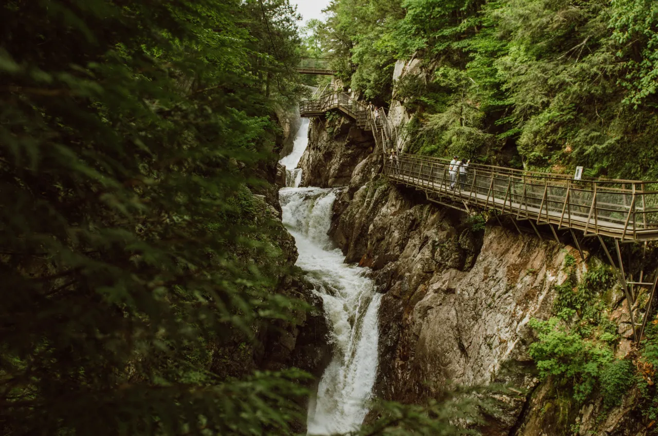 View of waterfall in lush green and rock canyon with boardwalk on right side