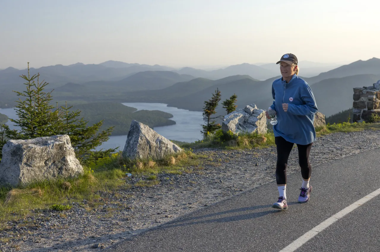 Woman in black leggings, blue shirt, and ball cap runs on mountain road