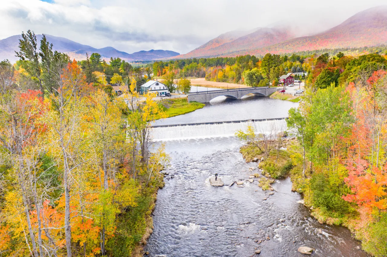 A bridge and dam in a small town surrounded by colorful fall foliage.