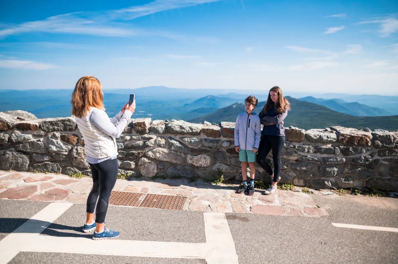 Mother takes photo of daughter and sun standing in front of mountain view