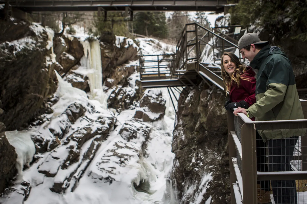 A man and woman look down at a gorge in winter. 