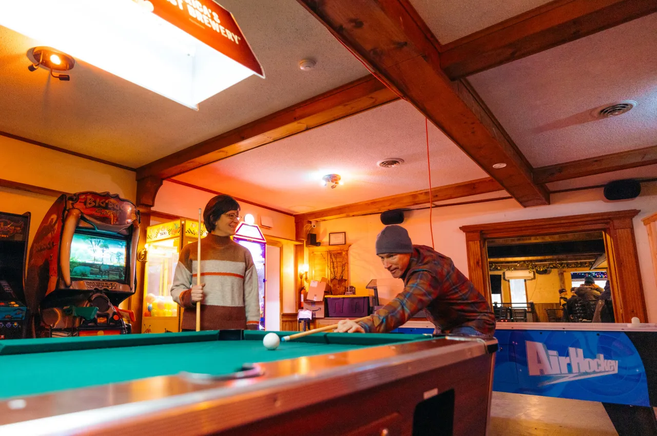 A man and woman play pool in a bar. 