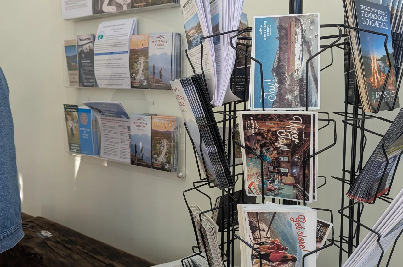 Rotatable rack of brochures sits on table in front of mounted brochure rack on white wall in Visitors and Business Center