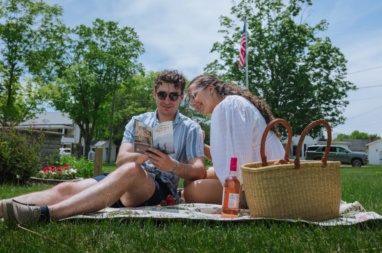couple sits on a blanket in a park in summer with a basket and bottle of wine looking together at Whiteface Region Guide