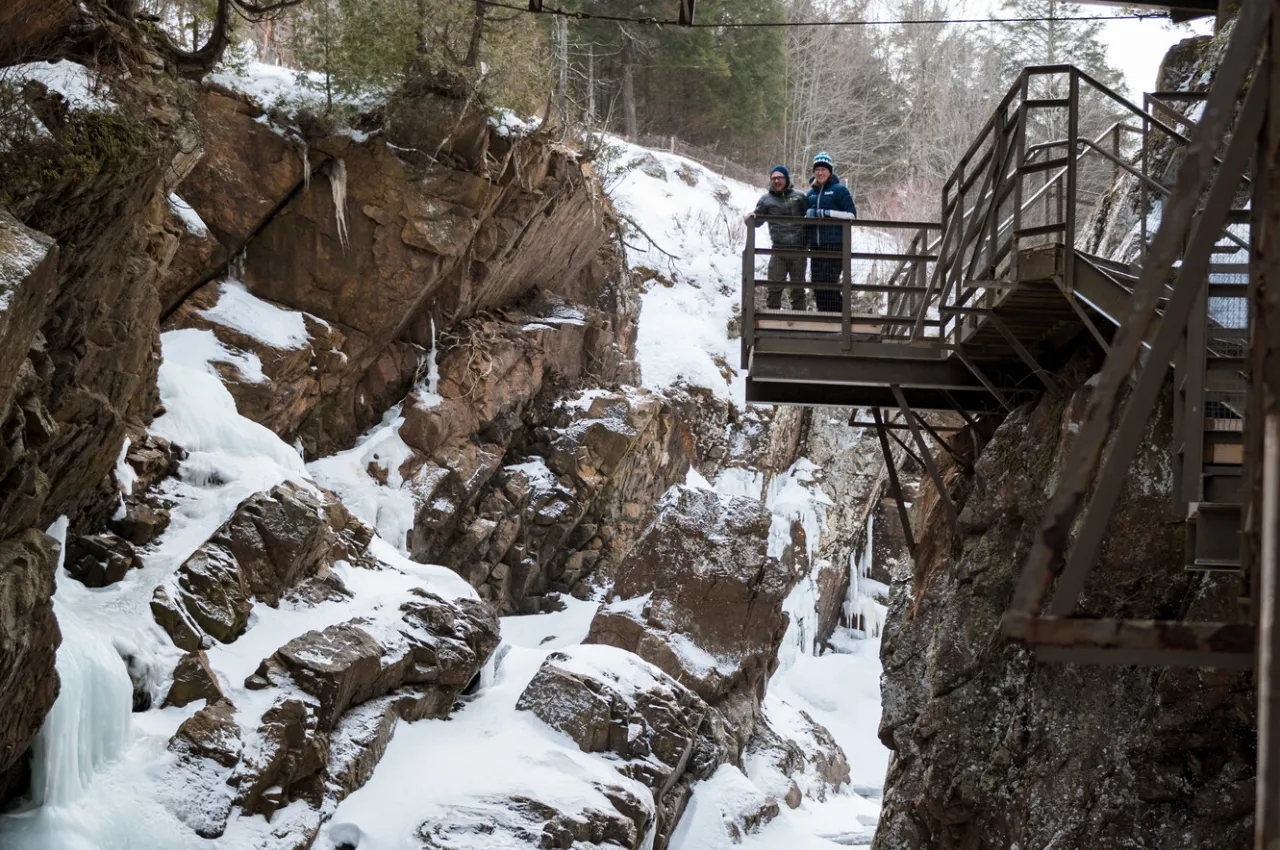 A couple stands on a platform overlooking a frozen over gorge. 