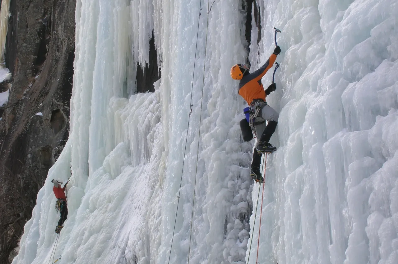 two men climb up an ice sheet on a mountain side. 
