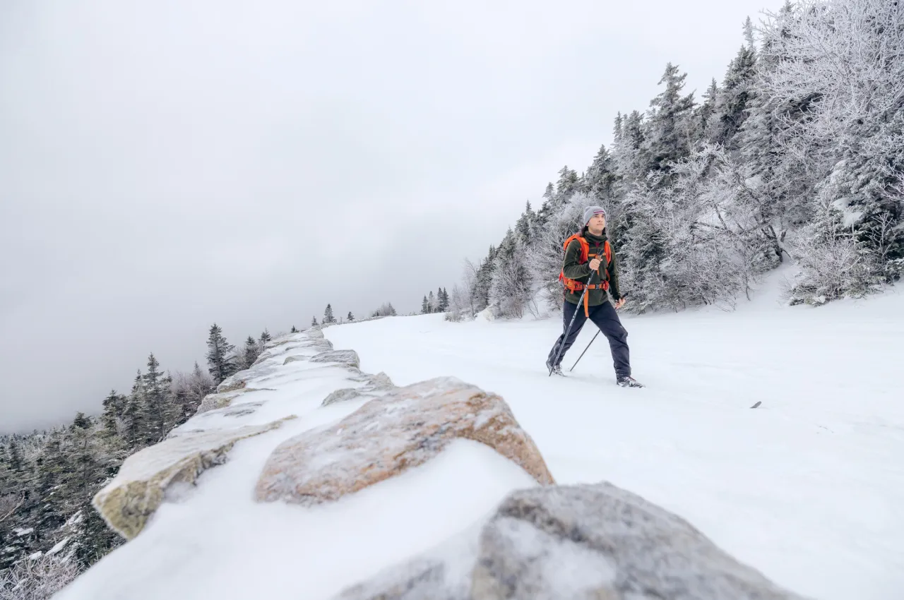 A man cross-country skis up a mountain trail in winter. 