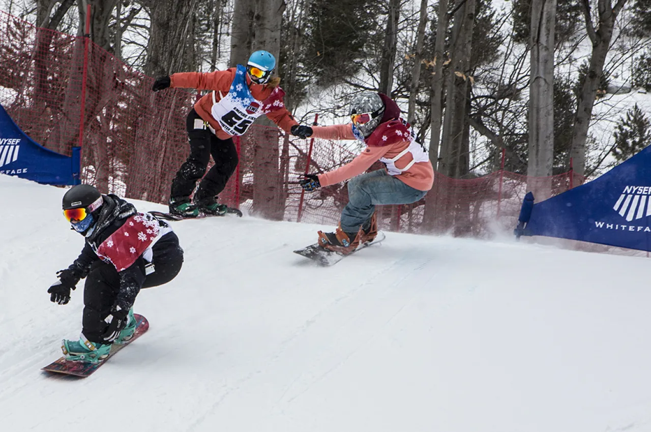 Three snowboard cross riders race down a snowy slope.