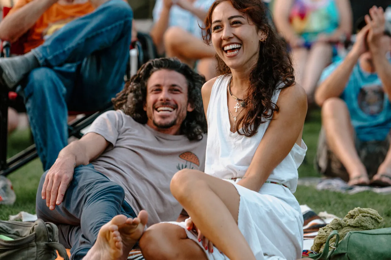 A man and woman laugh in a crowd at an outdoor concert.