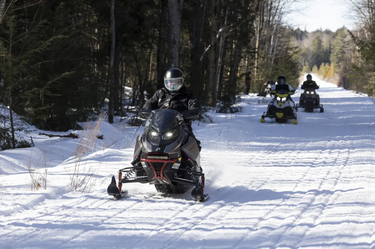 A group of snowmobilers ride down a snowy trail.