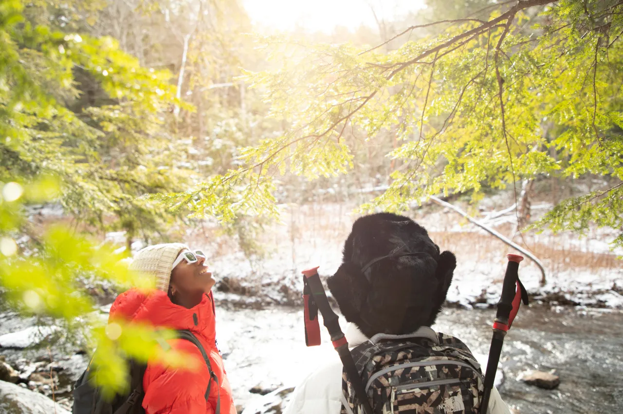 Two women in fuzzy hats look around at the winter scenery around them. 