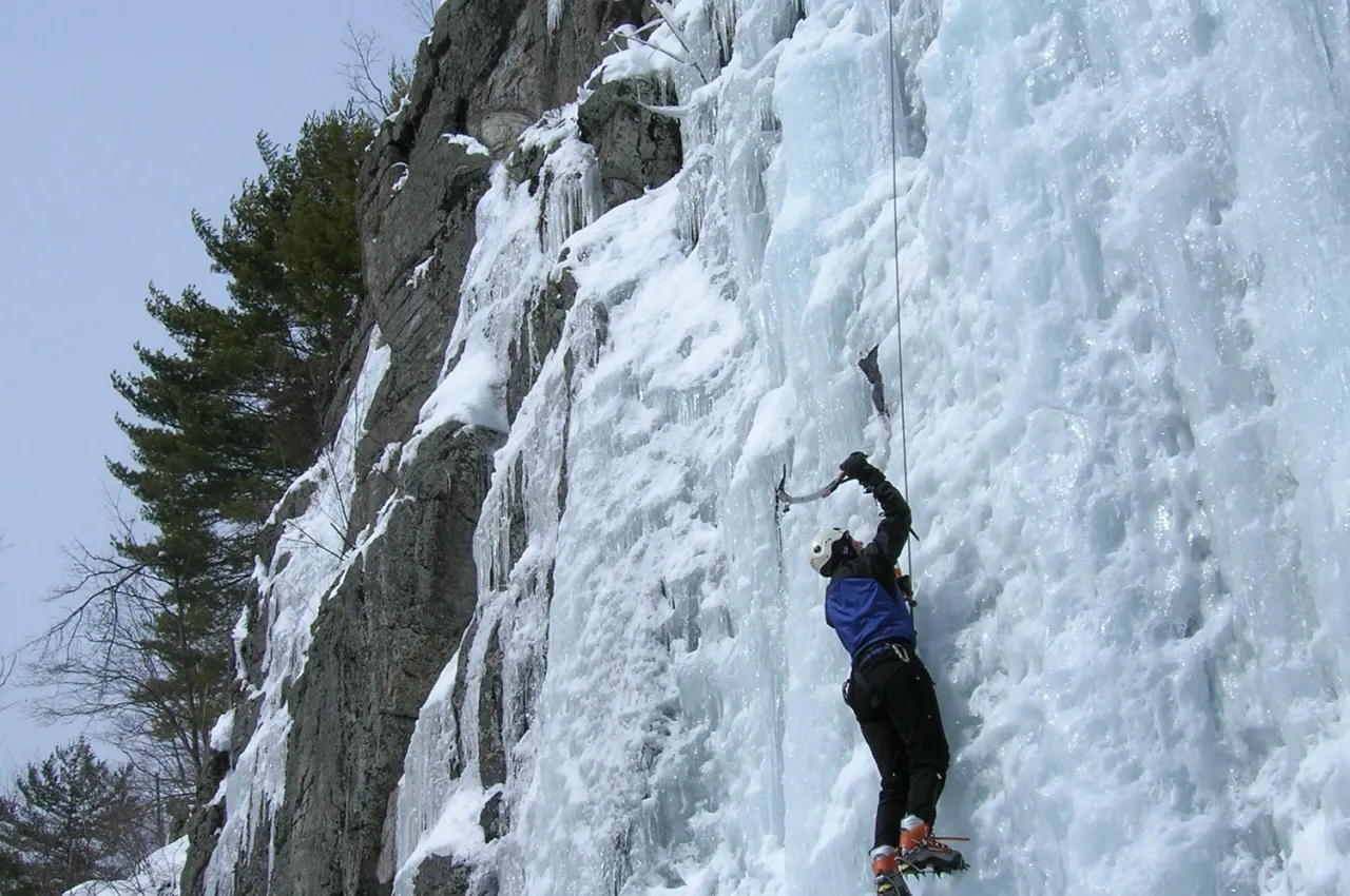 A man climbs an ice wall on a mountain with a pick. 