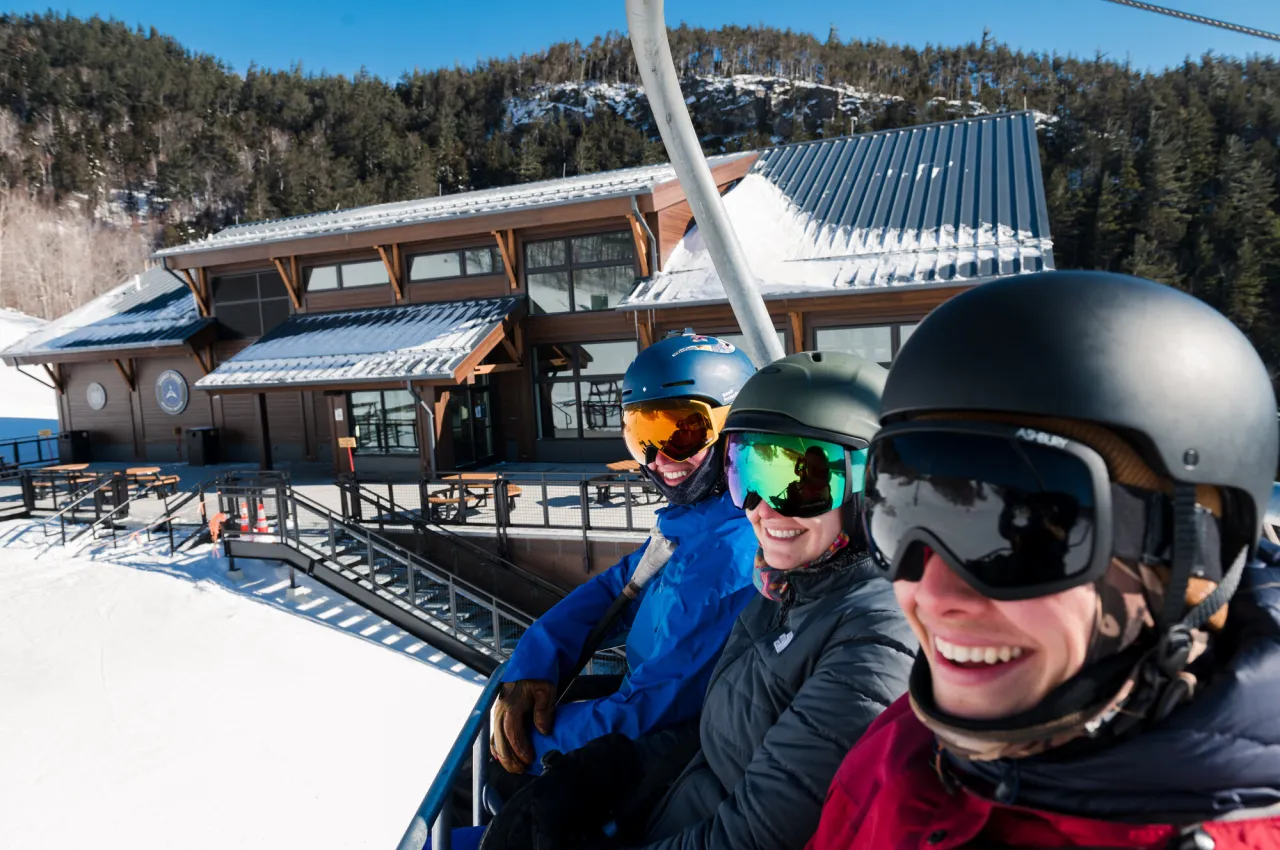 A group of three people smile in ski gear on a chair lift. 