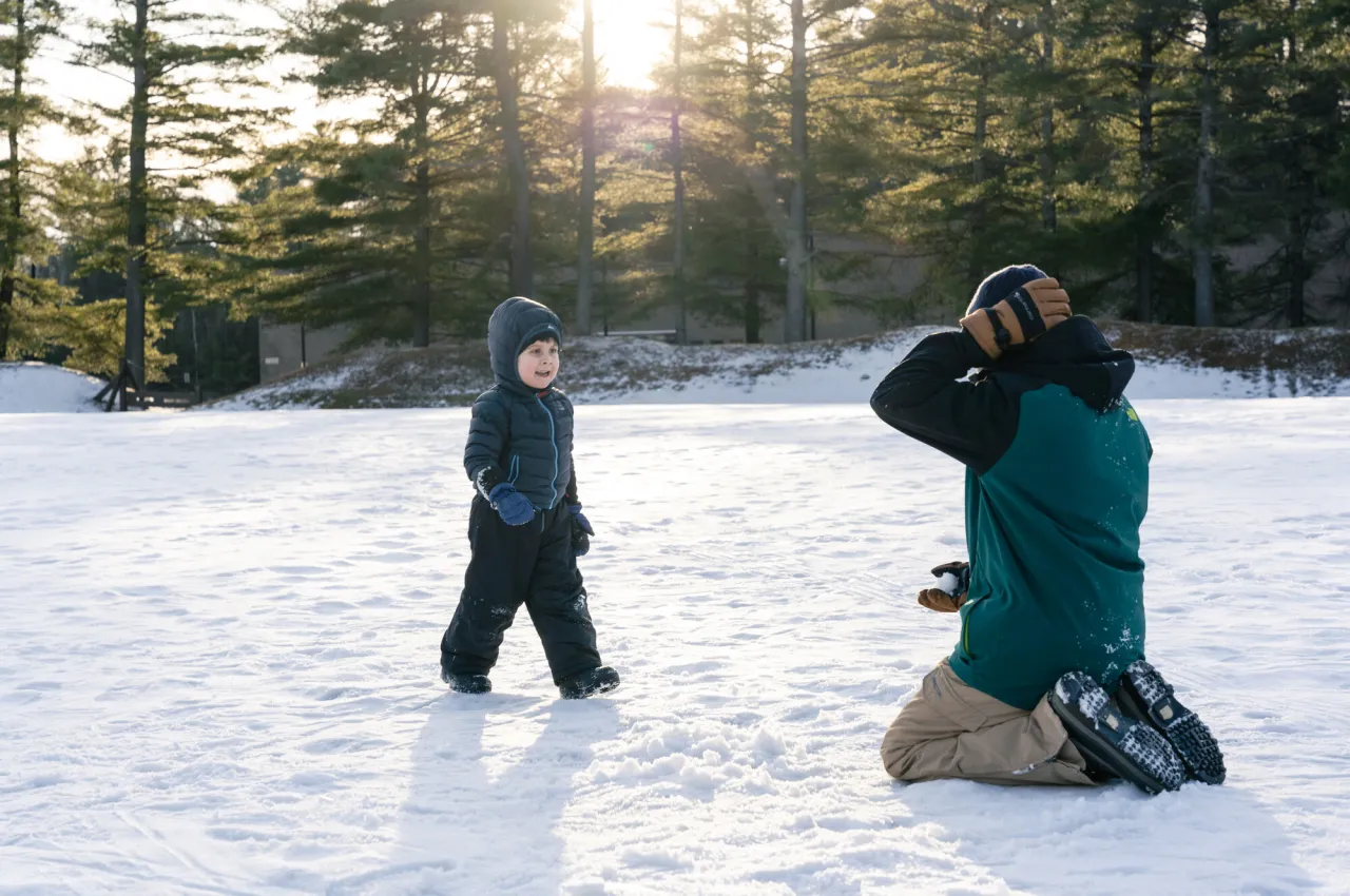 A man and his young son play in the snow in winter gear. 