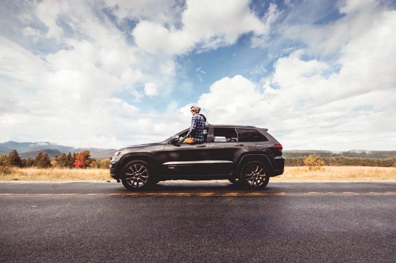 A man sits in the window of his SUV on a fall road.