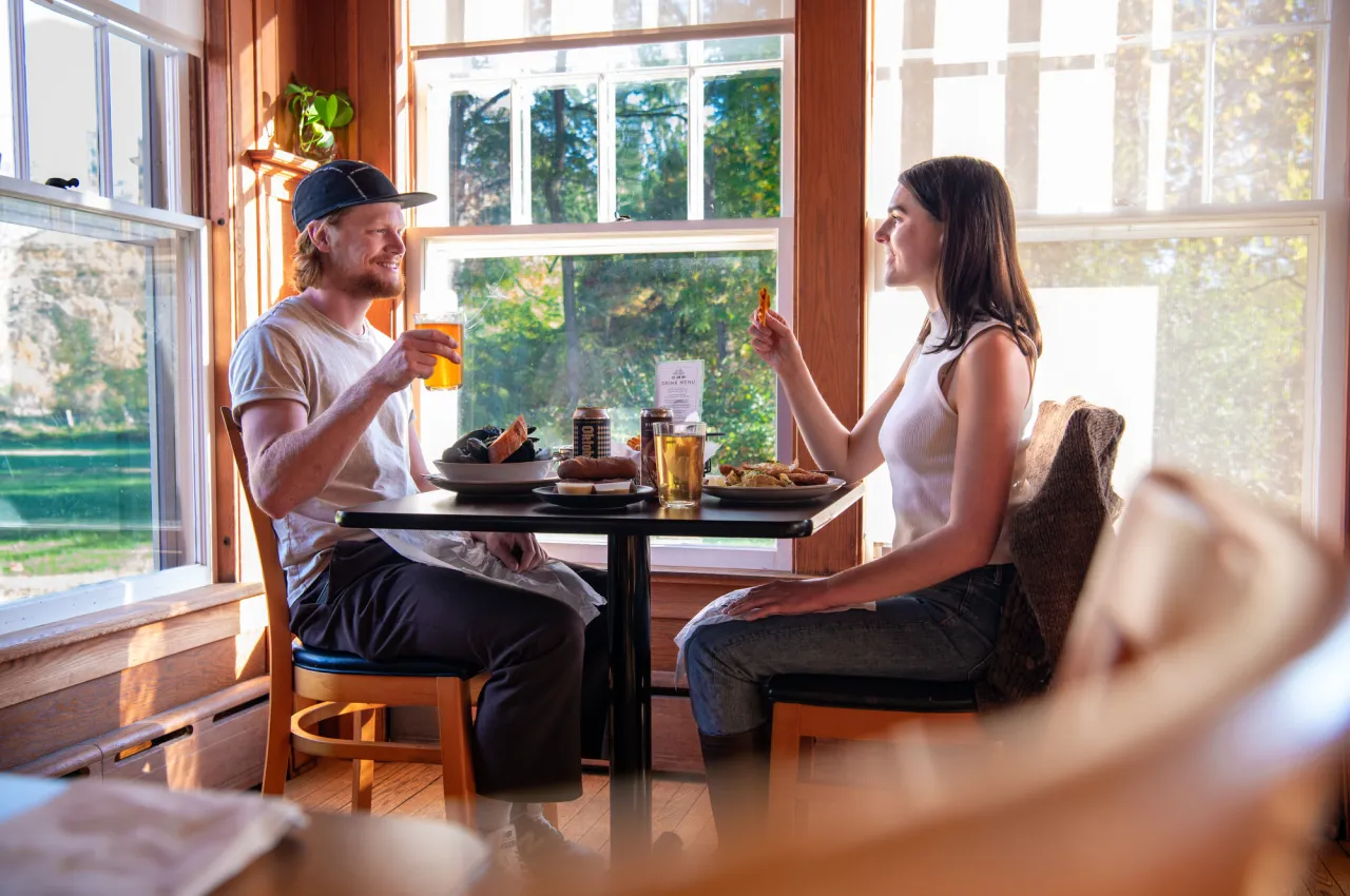 A man and woman share dinner at a rustic restaurant at a table next to a window. 