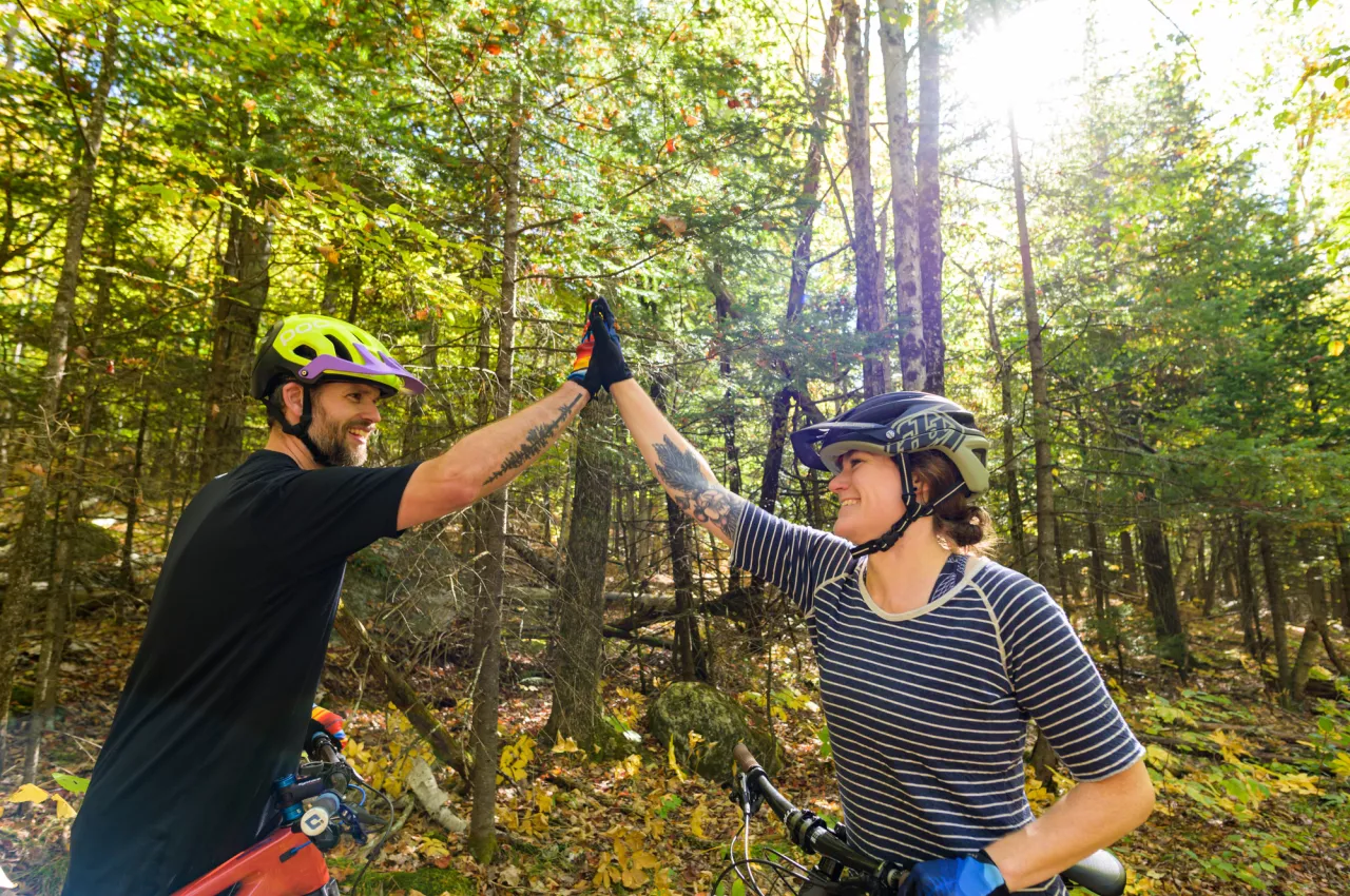 Two mountain bikers high five in the forest