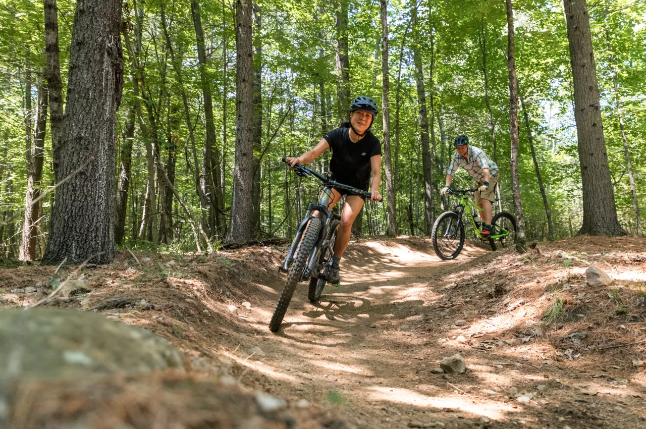 Two riders on mountain bikes on a forested trail in Wilmington