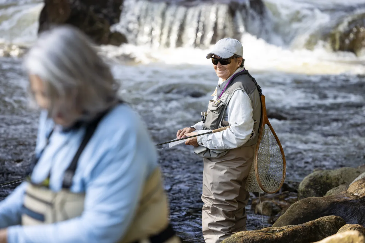 Two fly fishers stand in the river by a waterfall