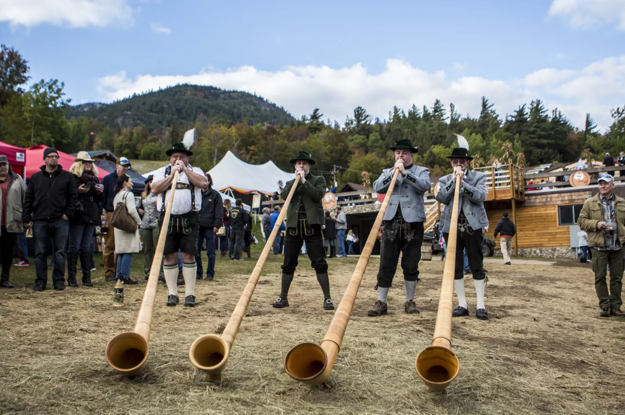 Men blow into horns at a fall festival.