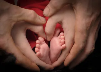 Teeny tiny baby feet are lovingly held by mom's hands in the shape of a heart with dad's hands on top of hers.