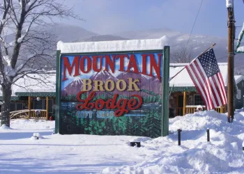 A sign reading Mountain Brook Lodge & Gift Shop among a snow covered space with large tree