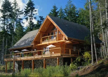 The exterior of a three story log cabin with wrap around deck and balcony above 