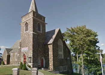 A tall stone church with high steeple on the banks of Mirror Lake.