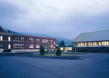 Brick school illuminated from within and surrounded by mountains.