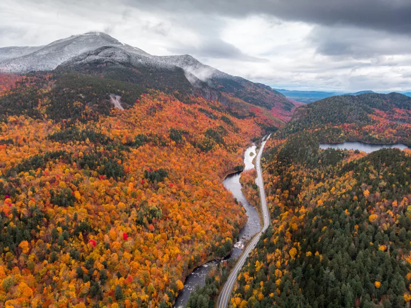 An aerial view of orange, yellow, and red trees with a snow-covered Whiteface Mountain in the background
