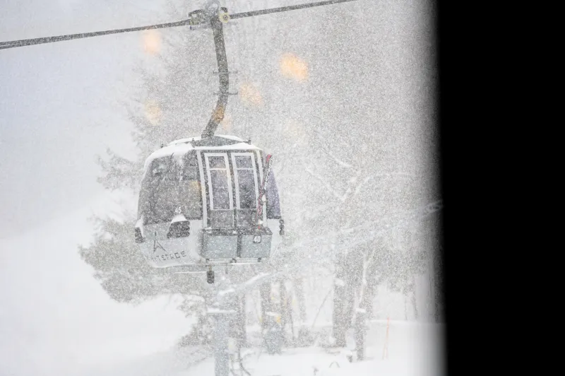 A gondola climbs up a mountain in heavy snow.