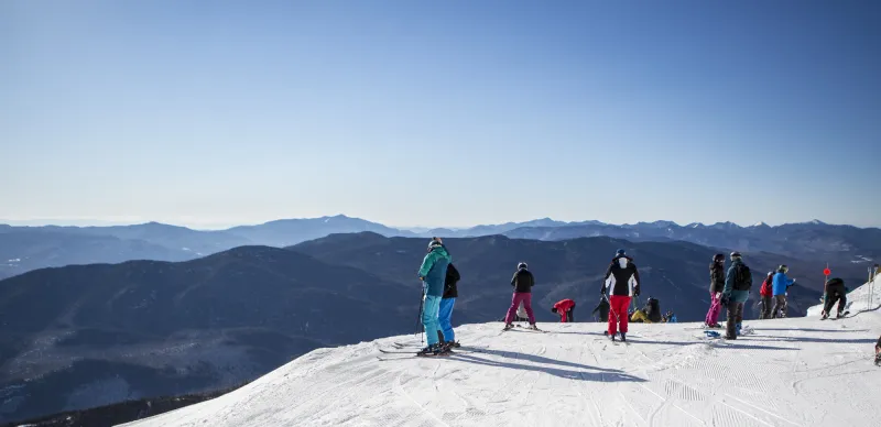 A group of skiers stand on top of a mountain.