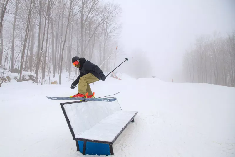 A skier rail sliding on a snowy day.