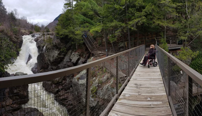 A woman in a wheelchair views the falls of High Falls Gorge from an accessible bridge.