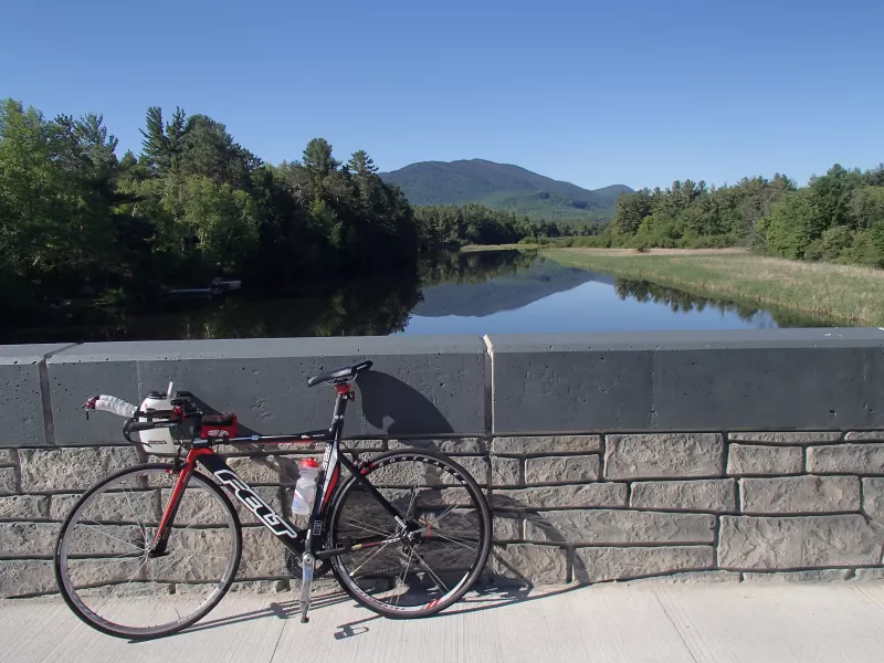 A road bicycle leans against a stone bridge overlooking a river.