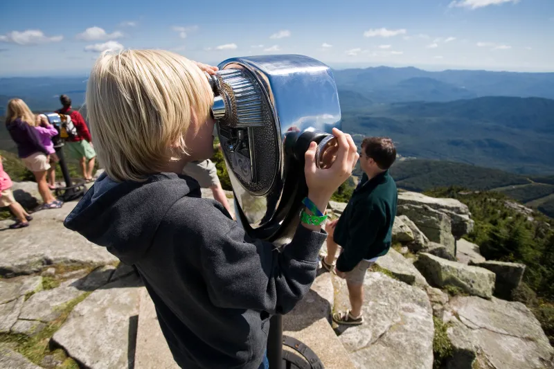A young boy looks through the telescope on the summit of Whiteface Mountain. The High Peaks are in the distance.