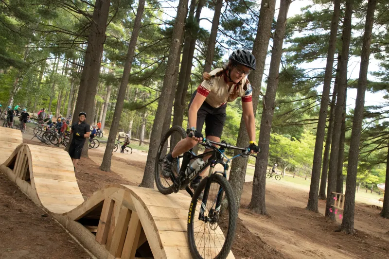 A woman bikes over a rolling, wooden feature at the Wilmington Bike Park
