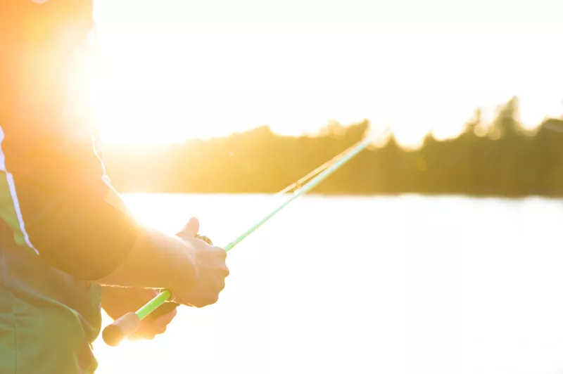 Close-up of someone holding a fishing rod with water and sunshine in the background