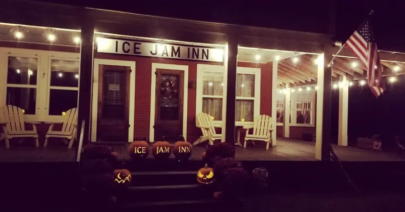 Exterior of the front porch of an inn, decorated with Adirondack chairs and jack-o-lanterns.